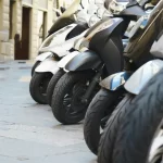 Describing a place in writing through repetition and routine: a row of parked scooters on a narrow city street.